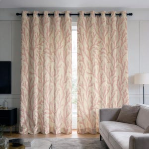 Può includere: Due pannelli di tenda beige con un motivo a corallo rosa. Le tende sono appese a un'asta nera con occhielli argentati. Sullo sfondo si vede un divano, e le tende sono davanti a una finestra.