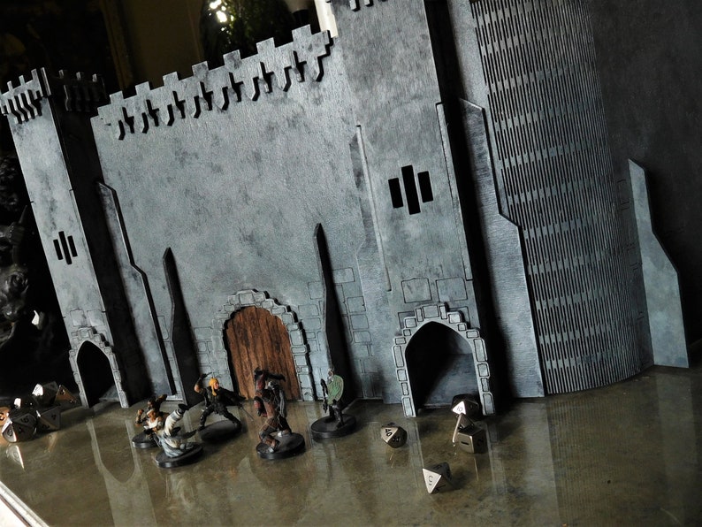 K&ouml;nnte beinhalten: Ein graues Schlossmodell mit einer Holzt&uuml;r und gew&ouml;lbten Durchg&auml;ngen. Vor dem Schloss befinden sich mehrere Miniaturfiguren und W&uuml;rfel.