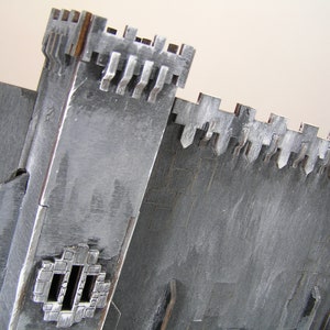 K&ouml;nnte beinhalten: Ein graues, h&ouml;lzernes Modell einer Burg mit einer Zinnenmauer und einem kleinen Fenster. Das Modell besteht aus mehreren zusammengef&uuml;gten Holzst&uuml;cken.