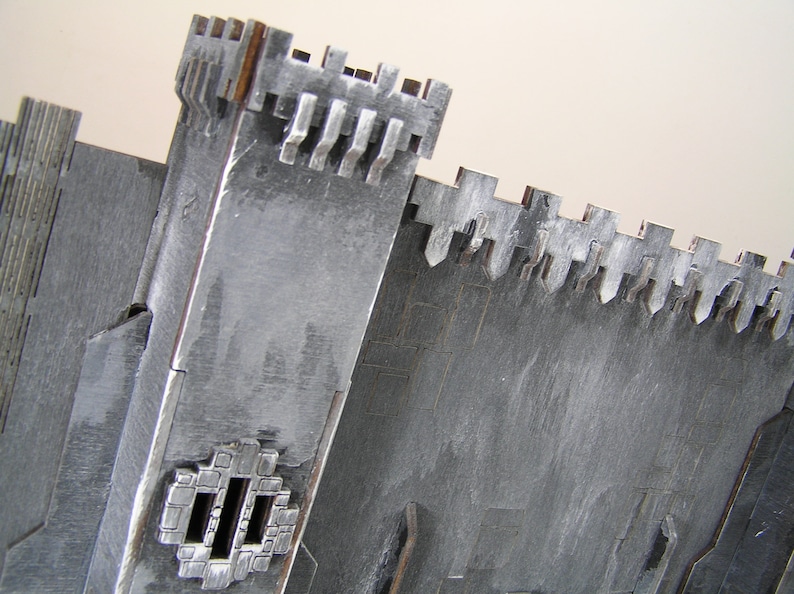 K&ouml;nnte beinhalten: Ein graues, h&ouml;lzernes Modell einer Burg mit einer Zinnenmauer und einem kleinen Fenster. Das Modell besteht aus mehreren zusammengef&uuml;gten Holzst&uuml;cken.