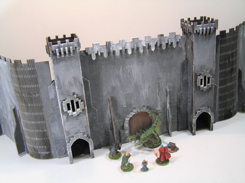 K&ouml;nnte beinhalten: Eine graue Steinburgmauer mit einer gro&szlig;en Holzt&uuml;r und einer gr&uuml;nen Drachenfigur davor. Vier Miniaturfiguren stehen vor der Burgmauer.