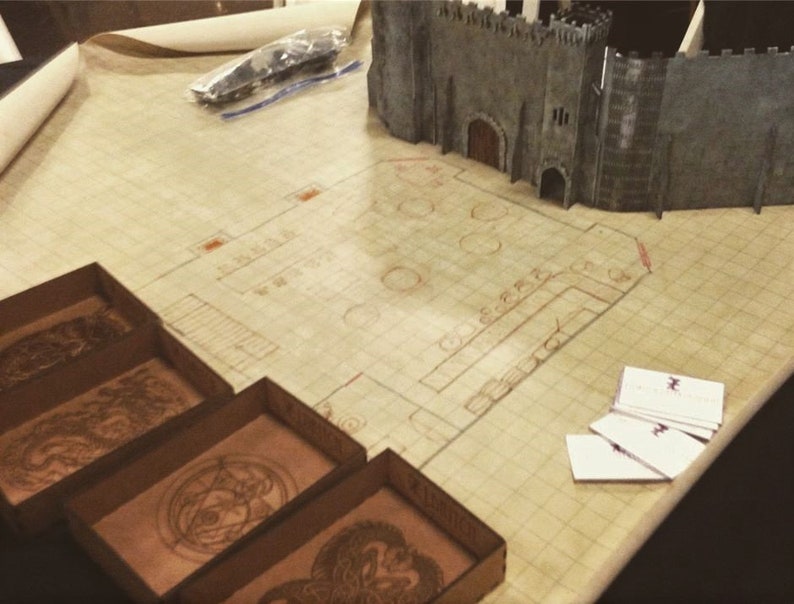 K&ouml;nnte beinhalten: Ein Tabletop-Spielset mit einer braunen Karte, einer grauen Schlossminiatur und vier kleinen Holzkisten mit aufwendigen Designs. Die Kisten sind mit den Worten "Drache", "Auge", "Drache" und "Drache" beschriftet.