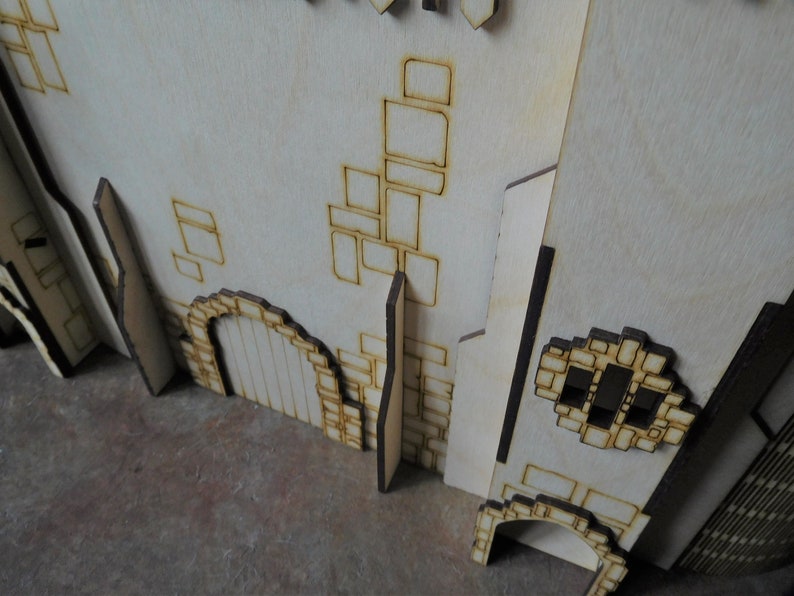 K&ouml;nnte beinhalten: Ein Holzmodell einer Burg mit einer Backsteinmauer, einer T&uuml;r und einem Fenster. Das Modell ist aus Sperrholz und hat eine hellbraune Farbe.