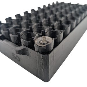 Puede incluir: Una bandeja de plástico negro con múltiples compartimentos cilíndricos. La bandeja está diseñada para contener objetos pequeños, con el número "50" visible en el lateral. Los compartimentos están dispuestos en filas y columnas, lo que sugiere un almacenamiento organizado.