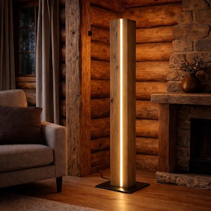 Könnte beinhalten: Eine hohe Holz-Stehlampe mit einem vertikalen, beleuchteten Lichtstreifen. Die Lampe besteht aus hellbraunem Holz und steht auf einem schwarzen Metallsockel. Sie befindet sich in einem rustikalen Raum mit Kamin und Holzwänden. Die Höhe beträgt ca. 180 cm.