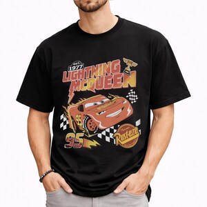 Puede incluir: Camiseta negra con un dise&ntilde;o de Rayo McQueen de la pel&iacute;cula Cars. El dise&ntilde;o incluye el texto "Lightning McQueen" en rojo y amarillo, el n&uacute;mero "95" y el logotipo de "Rusteze". La camiseta tiene un aspecto vintage y desgastado.
