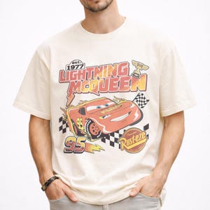 Puede incluir: Camiseta color crema con un dise&ntilde;o de Rayo McQueen de la pel&iacute;cula Cars. El dise&ntilde;o incluye el texto "Lightning McQueen" y "95" en rojo y amarillo, una bandera a cuadros y el texto "Rust-eze".