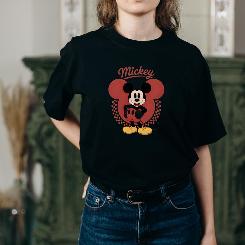 May include: Black t-shirt featuring a red Mickey Mouse graphic with the word "Mickey" above the character's head. The graphic includes a checkered pattern and yellow shoes. The shirt is made of a soft material.