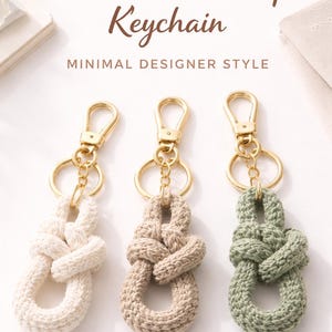 May include: Three crochet knot loop keychains in cream, tan, and sage green. Each keychain features a gold-colored clasp and ring. The text "Crochet Knot Loop Keychain" and "Minimal Designer Style" are displayed above the keychains.