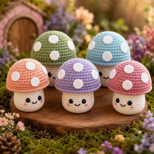 Op de afbeelding: Vijf gehaakte paddenstoel figuren in perzik, groen, paars, blauw en roze. Elke paddenstoel heeft een witte steel en een kap met witte stippen. De paddenstoelen hebben lachende gezichten en zijn gerangschikt op een houten oppervlak.