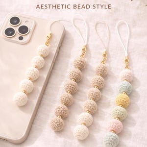 Puede incluir: Correas de encanto para teléfono de ganchillo en crema, beige y colores pastel. Cada correa presenta bolas de ganchillo con detalles dorados, unidas a un teléfono. El texto de la imagen dice "Crochet Phone Charm Strap" y "Aesthetic Bead Style."