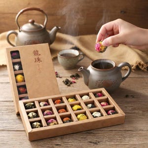 May include: A box of blooming tea balls in a cardboard box with the Chinese characters "龍珠" on the side. The tea balls are in various colors, including yellow, pink, and white. A teapot and teacup are in the background.