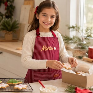 May include: A burgundy apron with thin white vertical stripes, featuring the embroidered name Maria in yellow cursive script next to a small white bird icon. The apron has adjustable red neck straps and a front pocket with a small brown label.