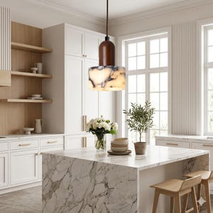 May include: A contemporary kitchen featuring a marble island and wooden stools. A pendant light with a brown wooden top and a white and grey patterned shade hangs above the island. White cabinets and shelves are in the background.