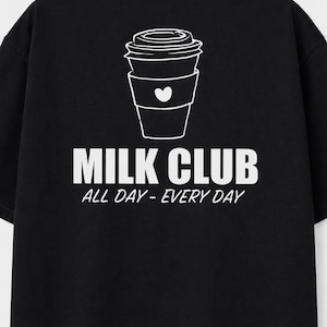 Könnte beinhalten: Schwarzes T-Shirt mit weißer Grafik einer Kaffeetasse mit Herz und den Worten "MILK CLUB" und "ALL DAY - EVERY DAY". Das Design befindet sich auf der Rückseite. Ein lässiges Kleidungsstück.