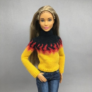 May include: A doll wearing a yellow, red, and black sweater with a turtleneck collar and long sleeves. The sweater has a flame-like design on the upper chest. The doll is also wearing blue jeans.