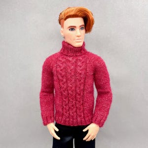 May include: A doll wearing a red turtleneck sweater with a cable knit design. The doll has red hair and is wearing black pants. The sweater is a deep shade of red, and the overall look is casual and stylish.