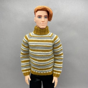 May include: A doll wearing a mustard yellow, gray, and white striped turtleneck sweater. The sweater has long sleeves and a ribbed collar. The doll has red hair and is wearing black pants.