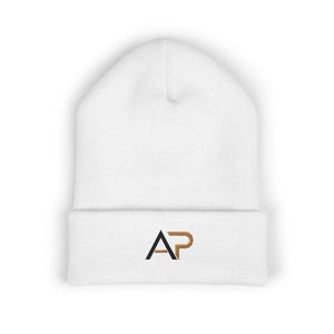 May include: A white beanie with a folded brim. The beanie features the embroidered letters "AP" in black and gold. The hat is made of a soft, knitted material, perfect for cold weather.