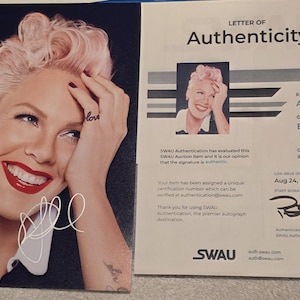 Könnte beinhalten: Signiertes Foto einer lächelnden Frau mit rosa Haaren und rotem Lippenstift. Ein Echtheitszertifikat von SWAU ist enthalten, das "Authentisch" und "Ausgezeichnet" ausweist.