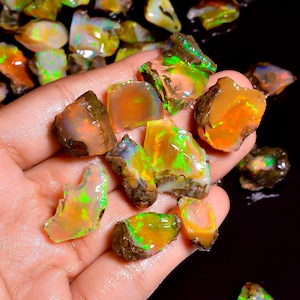 Op de afbeelding: Een verzameling ruwe, ongepolijste opaalstenen met doorschijnende, melkwitte basissen en levendige flitsen van neon-groen, oranje en geel vuur. De onregelmatige, grillige edelstenen vertonen een natuurlijke, ruwe textuur en gevarieerde vormen.