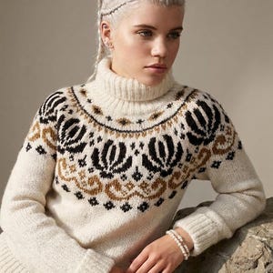 Könnte beinhalten: Ein cremefarbener Rollkragenpullover mit einem detaillierten Muster in Schwarz und Braun an der Passe. Das Strickkleidungsstück hat lange Ärmel mit gerippten Bündchen, einen gerippten Kragen und einen gerippten Saum mit floralem Muster.
