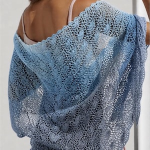 Peut inclure: Un châle bleu crocheté avec un effet dégradé, passant du clair au foncé. Le châle présente un motif ajouré délicat, créant une texture dentelle. Le vêtement est drapé sur les épaules.