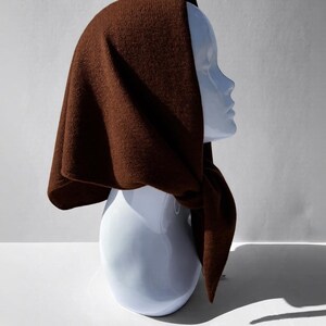 Pode incluir: Um capuz de malha castanho, drapeado sobre uma cabe&ccedil;a de manequim branca. O capuz &eacute; de cor castanha quente e lisa e parece ser feito de um material macio e texturizado. O capuz &eacute; amarrado no pesco&ccedil;o, com as pontas penduradas.