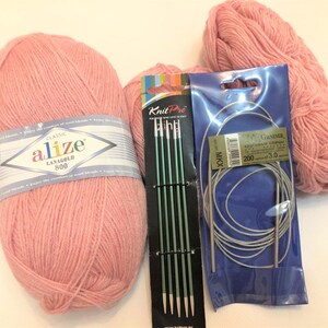 Pode incluir: Uma cole&ccedil;&atilde;o de materiais de tric&ocirc; rosa, incluindo dois novelos de l&atilde;, um conjunto de agulhas de tric&ocirc; verdes e um conjunto de agulhas de tric&ocirc; circulares. A l&atilde; &eacute; rotulada como "Alize Lanagold 800".