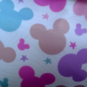 May include: A white fabric with a repeating pattern of Mickey Mouse silhouettes in various colors, including pink, purple, blue, and peach. Small star shapes are scattered throughout the design. The fabric has a subtle, wavy texture.