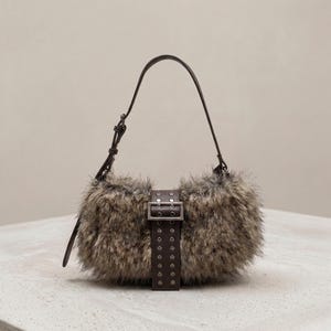 May include: A small, fluffy handbag with a brown leather strap and buckle. The bag is covered in faux fur in shades of brown and gray. The strap is attached to the bag with a metal buckle.