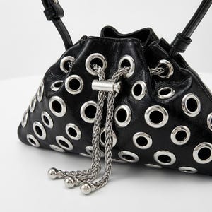 Può includere: Borsa a secchiello in pelle nera con occhielli argentati e chiusura con coulisse a catena argentata. La borsa ha un cinturino in pelle nera e dettagli a sfera argentati sulla coulisse. Un accessorio moda unico.