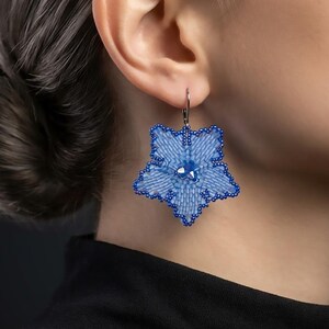 May include: A star-shaped dangle earring crafted from light blue seed beads with a dark blue beaded border. The center features three small, faceted dark blue crystals. The earring hangs from a simple silver-toned metal hook wire.