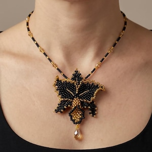 May include: A beaded necklace featuring a large, intricate black and gold floral-shaped pendant. The pendant is crafted from small seed beads with a central gold cluster and a dangling teardrop crystal. The chain consists of black and gold beads.