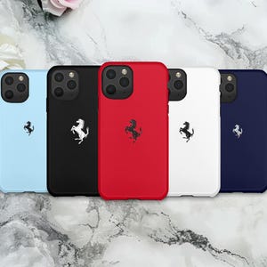 Könnte beinhalten: Fünf Telefonhüllen in verschiedenen Farben: Hellblau, Schwarz, Rot, Weiß und Marineblau. Jede Hülle hat ein schwarzes Pferdelogo. Die Hüllen liegen auf einer Marmoroberfläche.