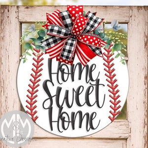 Op de afbeelding: Een rond wit bord met een honkbalthema, met rode stiksels en de tekst "Home Sweet Home" in zwarte letters. Het is versierd met een rood, zwart en witte strik en groen.