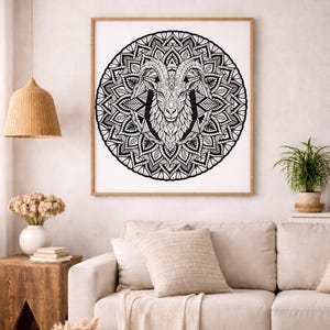 May include: Black and white framed art print featuring a detailed mandala design with a ram's head at the center. The artwork is displayed in a living room setting, above a beige sofa. The print is in a wooden frame.
