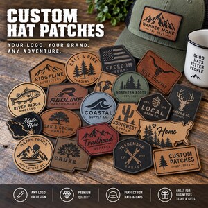 May include: A collection of custom leather and synthetic patches in various shapes and sizes, featuring engraved logos, mountain scenes, trees, animals, and text. The patches are arranged on a wooden surface next to a green baseball cap and a white mug.