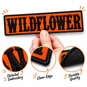 May include: A rectangular embroidered patch featuring the word WILDFLOWER in bold black lettering on a bright orange background. The patch has a black stitched border and is shown with close-up circular insets highlighting the embroidery.