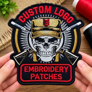 May include: A black embroidered patch featuring a white skull wearing a tan military cap with red chevron details. The text CUSTOM LOGO is arched above, and EMBROIDERY PATCHES is in a red rectangle below. Two rifles are crossed behind the skull.