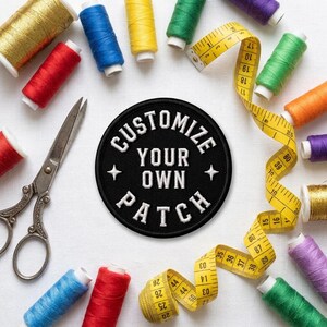 K&ouml;nnte beinhalten: Ein runder, schwarz bestickter Aufn&auml;her mit dem wei&szlig;en Text CUSTOMIZE YOUR OWN PATCH, umgeben von verschiedenen bunten Garnrollen, einer Metallschere und einem gelben Ma&szlig;band mit metrischen Markierungen.