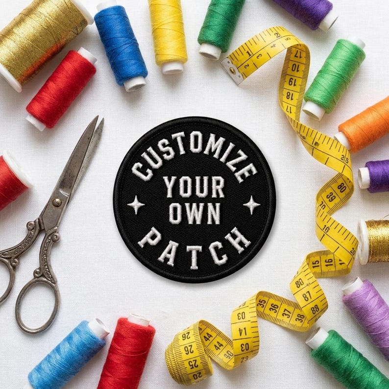 K&ouml;nnte beinhalten: Ein runder, schwarz bestickter Aufn&auml;her mit dem wei&szlig;en Text CUSTOMIZE YOUR OWN PATCH, umgeben von verschiedenen bunten Garnrollen, einer Metallschere und einem gelben Ma&szlig;band mit metrischen Markierungen.