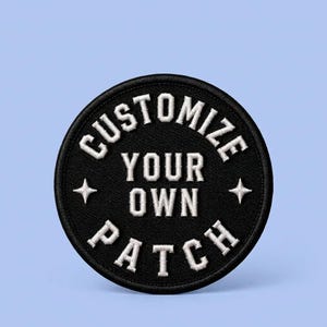 K&ouml;nnte beinhalten: Ein kreisf&ouml;rmiger, schwarz bestickter Aufn&auml;her mit wei&szlig;em, gesticktem Text, der in fetter Schrift CUSTOMIZE YOUR OWN PATCH lautet. Das Design enth&auml;lt zwei kleine vierzackige Sternsymbole links und rechts vom zentralen Text.