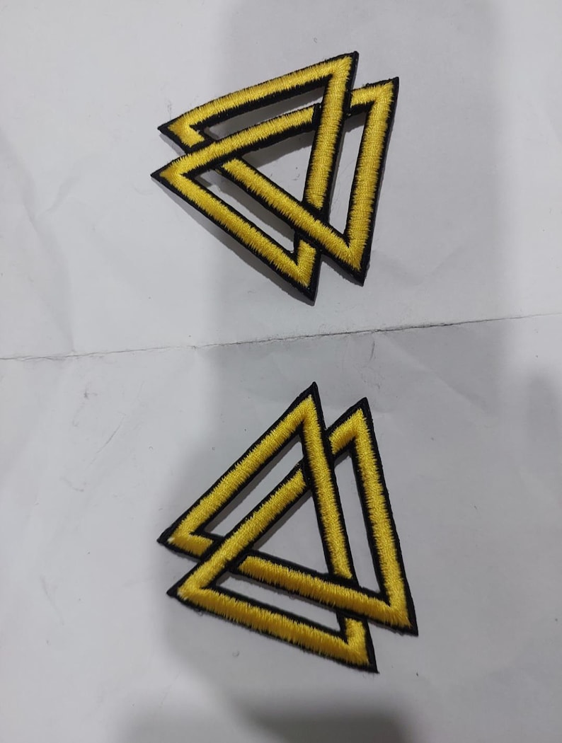 May include: Two embroidered patches, each featuring a yellow triangle design with a thick black border. The geometric pattern consists of two overlapping triangles, creating an interlocking effect with bright yellow thread and black stitching.