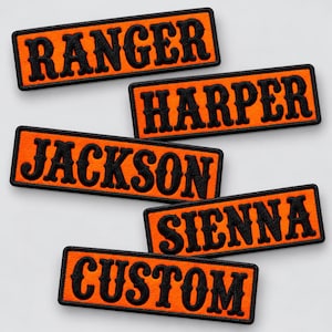 May include: Five rectangular embroidered patches with bright orange backgrounds and black borders. Each patch features black text in a bold, serif font. The names displayed are RANGER, HARPER, JACKSON, SIENNA, and the word CUSTOM.