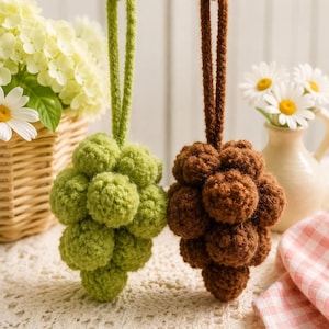 May include: Two hanging ornaments shaped like clusters of grapes, each crafted from multiple crocheted spheres. One cluster is light green and the other is dark brown. Each ornament features a matching crocheted loop for hanging purposes.