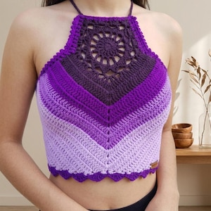 May include: A handcrafted, halter-neck crochet top in shades of purple. The top has a geometric design with a scalloped edge and a central circular pattern. The colour gradient transitions from light to dark purple.
