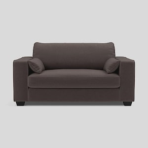 May include: A dark brown, two-cushion armchair with two matching throw pillows. The chair has a boxy shape with a low back and wide armrests. The legs are short and black. The fabric appears to be a textured weave.