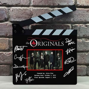 以下が含まれることがあります： 白い文字で「The Originals」と書かれ、中央に赤い枠で囲まれたキャストの写真がある黒い映画用カチンコ。ボードには白い印刷のサインと、「Created by: Julie Plec」、「Release Date: October 3, 2013」、「Final Episode: August 1, 2018」というテキストが含まれています。