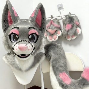 May include: A gray and white furry wolf fursuit head, paws, and tail set. The head has large, expressive eyes, pink accents, and a studded muzzle. The paws are gray with pink paw pads, and the tail is gray with pink details.